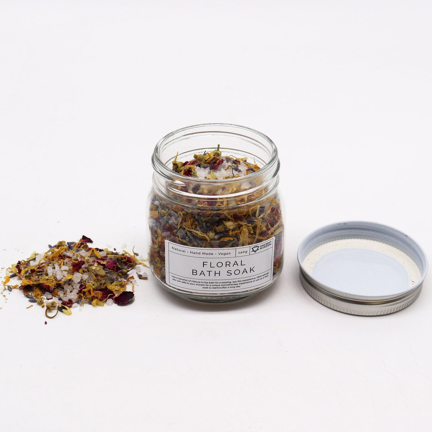 Blumiges Badesalz mit Blüten – geöffnetes Glasgefäß mit Deckel und Inhalt daneben