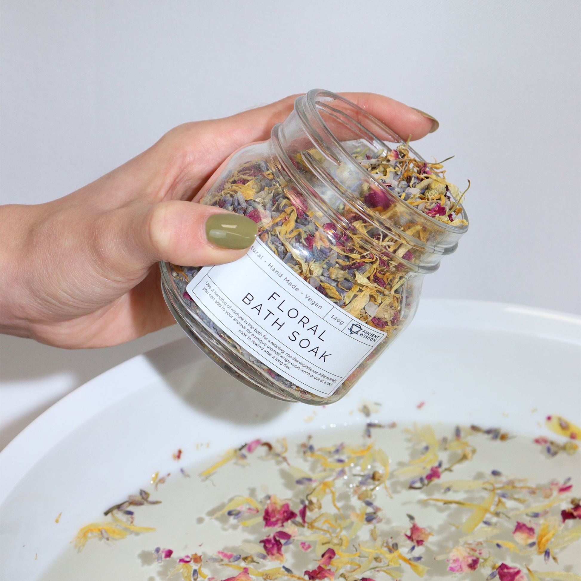 Blumiges Badesalz mit Blüten – wird in Badewanne eingegossen, Hand hält Glasgefäß